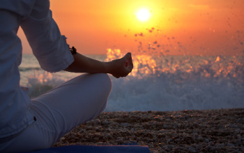 Woman facing the sunset on the beach while meditating.  Meditating is one element of creative visualization techniques you can use.
