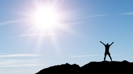 Man standing on a mountain greeting the sun.  This photo represents how vibrational energy healing can leave a person feeling refreshed.